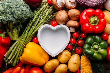 Top view of a wooden table full of vegetables and in the middle of the image an empty heart shaped dish, conceptual photo, food lover