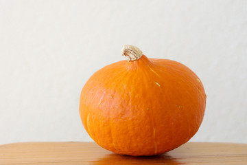 Small Round Ripe Vivid Orange Heirloom Hokkaido Pumpkin on Wooden Kitchen Table. White Wall Background. Country Style. Cozy Rural Fall Autumn Atmosphere. Warm Soft Colors. Thanksgiving. Poster