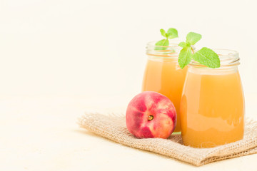 Peach smoothie in glass jars with fresh ripe fruits and green mint leaves on yellow pastel background.