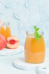 Peach smoothie in glass jars with fresh ripe fruits and green mint leaves on blue pastel background.
