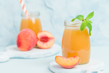 Peach smoothie in glass jars with fresh ripe fruits and green mint leaves on blue pastel background.