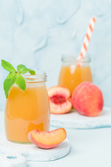 Peach smoothie in glass jars with fresh ripe fruits and green mint leaves on blue pastel background.
