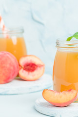 Peach smoothie in glass jars with fresh ripe fruits and green mint leaves on blue pastel background.