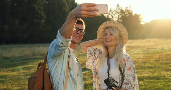 Close up of the joyful young boyfriend and girlfriend taking nice selfie photos on the smartphone camera and kissing in the beautiful nature in the field.
