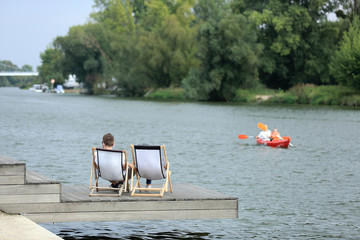 Dwoje ludzi wypoczywa na leżakach nad rzeką Odrą we Wrocławiu. - obrazy, fototapety, plakaty