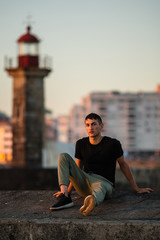 Fototapeta na wymiar Young man sitting near the sea lighthouse on the promenade at sunset time.