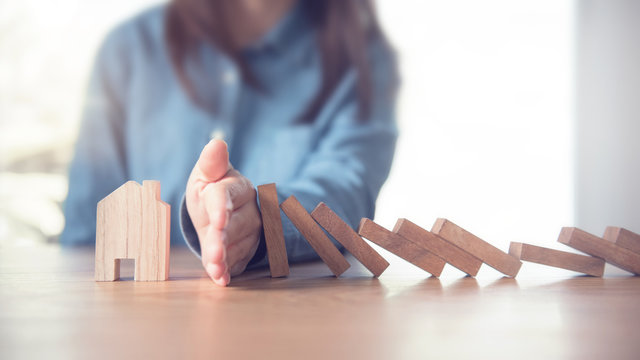 Woman hand stopping risk the wooden blocks from falling on house, Home insurance and security concept.
