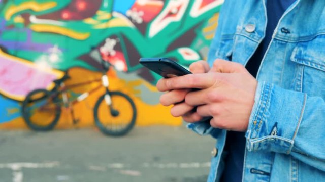 Close up of male hands with a smartphone with a bike and a graffiti in the background