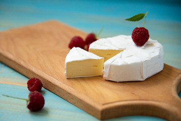 cheese camembert with raspberries and grapes on blue background