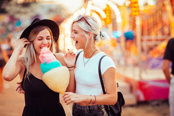 Shot of happy female friends in amusement park eating cotton candy. Two young women enjoying a day...