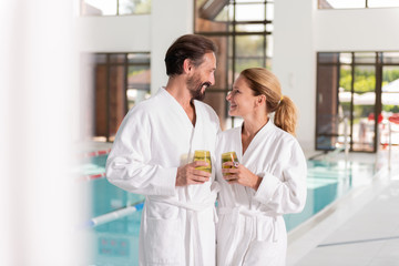 Time together. Delighted nice couple holding their tasty drinks while looking at each other