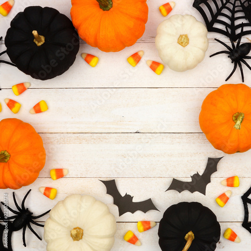 Halloween frame with black, orange and white decor and candy over a white wood background. Top view with copy space.
