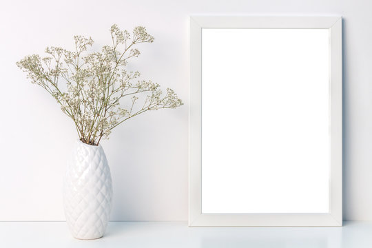 Desk with a white frame mockup with a vase with dried field flowers