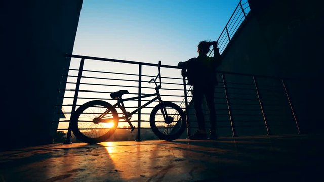 Male teenager is messing with his hair while standing on a platform with his bike in the sunset