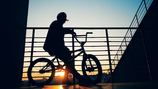 Male teenager is sitting on his bicycle in the rays of the setting sun and taking off his hat