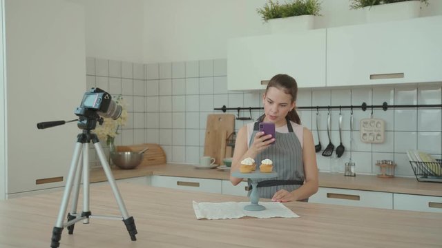 Confectionery blog. Housewife cooked cakes, put them on a stand and photographed them to make a post in blog. Pastry vlog. Confectioner decorates the capcake and then takes pictures on the smartphone