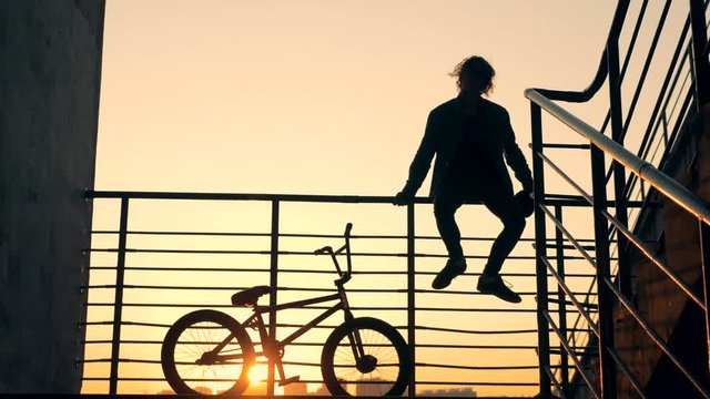 Staircase railing with a male adolescent sitting on it and his bicycle beside him