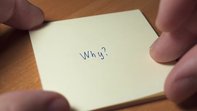 Hand is writing question WHY? on a sticker paper. Selective focus