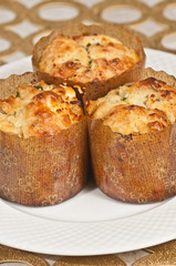 Top view, close up, three, freshly baked, homemade, hot, goat cheese herb muffins, in paper forms, on round, white plate, on a gold, circular placemat, vertical
