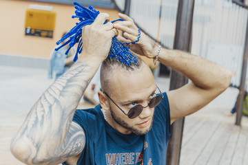 Young attractive man with blue dreadlocks touching his hair.