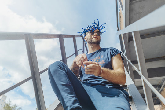 Young attractive man with blue dreadlocks sitting on staircase and shaking his hair.