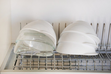 Obraz na płótnie Canvas Bright clean and washed glass and ceramic bowls on metal rack inside kitchen cupboard. Modern kitchen with tableware drying.