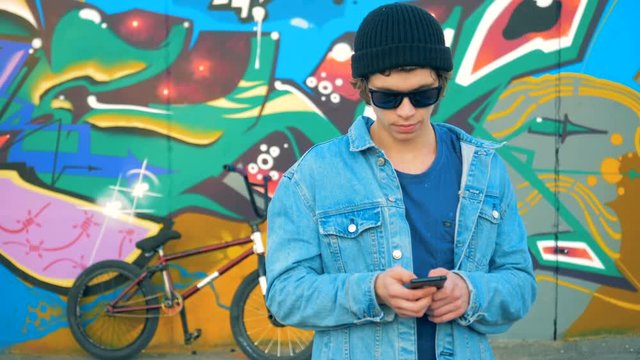 Street wall covered with graffiti and a male teenager with a smartphone near it