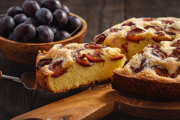 Homemade plum cake on dark wooden background.