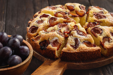 Homemade plum cake on dark wooden background.