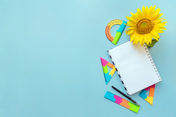 School open white notebook and sunflower on blue background, spiral notepad on a table. Still life, business, office, education concept, mock up