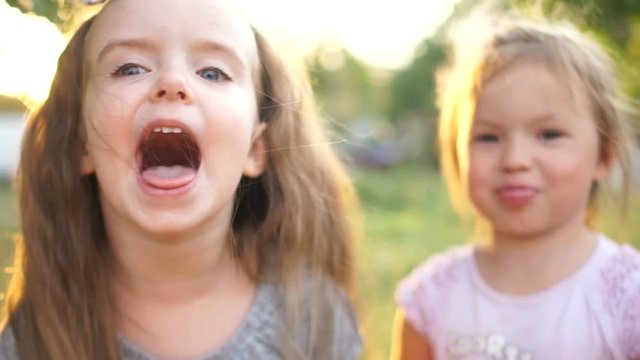 A little girl with long hair screams with joy. Next to her, her friend spits and shows her tongue. children fool around. All fools day