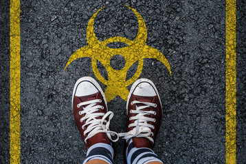 man legs in sneakers standing on asphalt road and biohazard sign