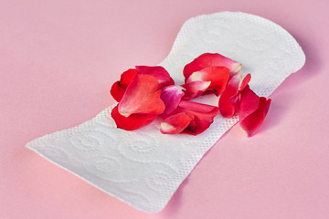 Sanitary napkin and flower petals on pink background
