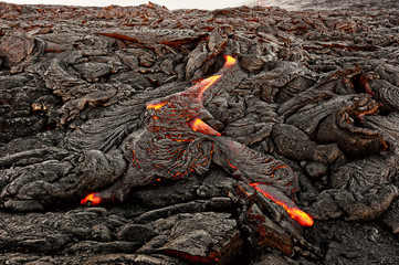 A lava flow emerges from an earth column and flows in a black volcanic landscape, in the sky shows...
