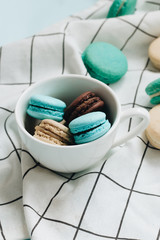 Composition of delicious macaroons in cup on blue table, sweet dessert