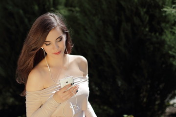 young pretty girl in light dress with open shoulders is listening music in headphones, open nature 