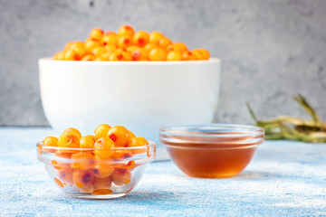 Sea-buckthorn berries in bowl and natural honey or sea buckthorn oil on blue background
