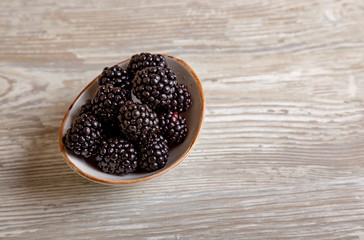 Blackberries in bowl on white wooden background, top view