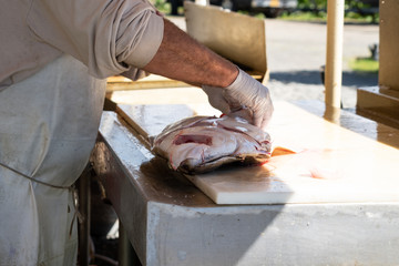 Male fisherman filets and processes a freshly caught halibut fish in Alaska
