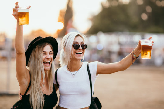 Two female friends drinking beer and having fun at music festival 
