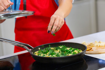 woman chef preparing omelette with herbs at a kitchen. Hands close up