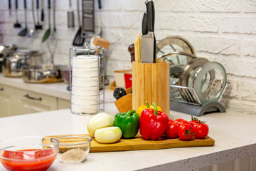 Kitchen knives in a special wooden stand with spice jars and fresh vegetables lie on a wooden board. Close-up. Kitchen concept