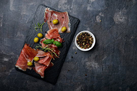 Meat plate, thin slices  of prosciutto or spanish jamon with olives on  stone cutting board, top view, copy space