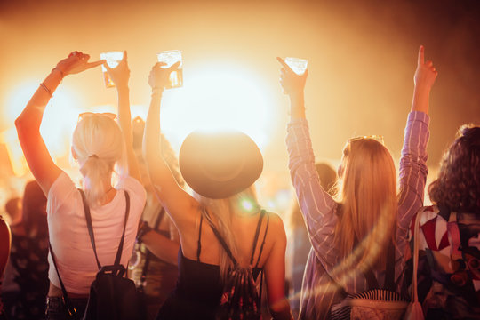 Back view of group of female friends at music festival drinking beer and dancing 