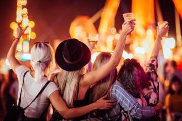 Back view of group of female friends at music festival drinking beer and dancing  - obrazy, fototapety, plakaty