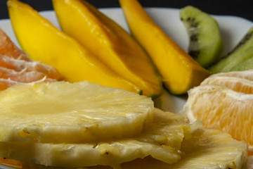 Tropical fruits, kiwi, mango, pineapple, orange and mandarin orange slices placed on white plate. Close up, macro photo.