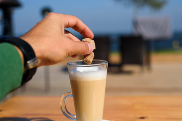 Man throws cubes of sugar cane in a mug of latte