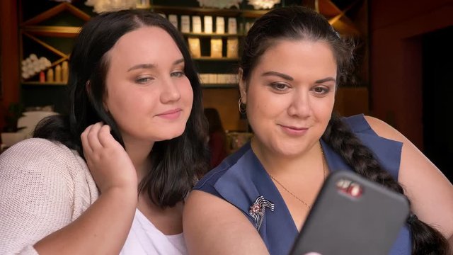 Two obese caucasian girlfriends taking photo on planshet in cafe with smirks on faces