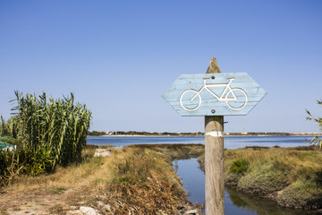 Wooden signpost for biking trails with arrows pointing direction of the road. Rural environment close to estuary water.