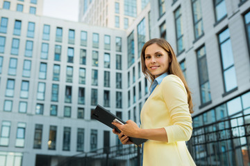 Fototapeta premium beautiful young girl with a folder of documents in hands in a yellow jacket against a building background
